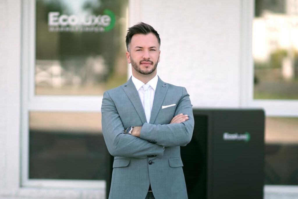 Ein gut gekleideter Mann mit ernstem Blick steht in einem grauen Anzug vor Ecoluxe